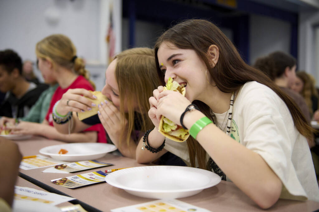 Teen student eating garlic aioli wrap in lunchroom