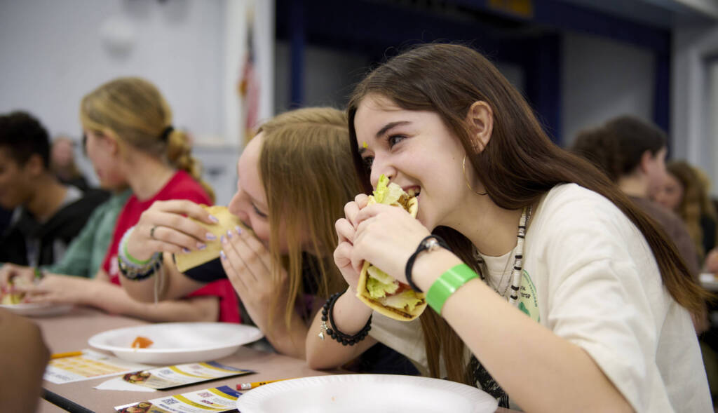 Teen student eating garlic aioli wrap in lunchroom